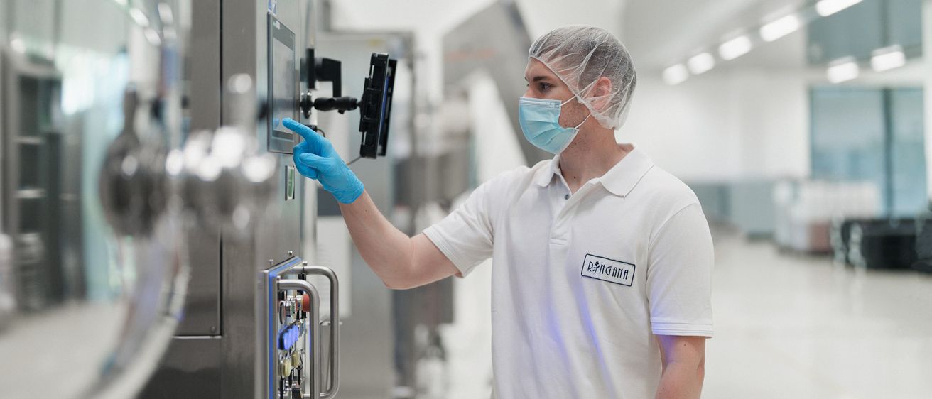 Ein Mann in Laborkittel und Gesichtsmaske bedient eine Kontrolltafel in einem Labor.