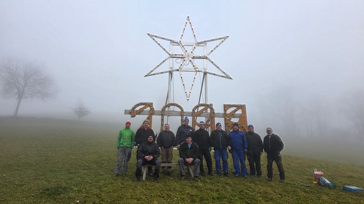 Eine Gruppe von Menschen steht vor einer großen sternförmigen Struktur mit Lichtern auf einem nebligen Feld.