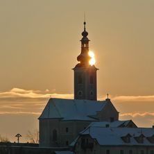 Die Sonne geht hinter einem Kirchturm unter und erhellt ihn, während sie ein warmes Licht auf die verschneiten Dächer wirft.