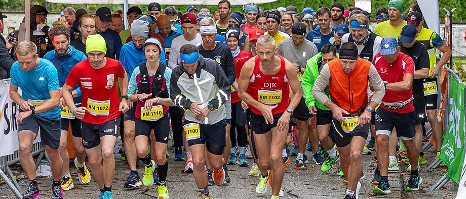 Läufer am Start eines Marathonlaufs, mit Nummern und farbenfroher Sportausrüstung, mit Zuschauern im Hintergrund.