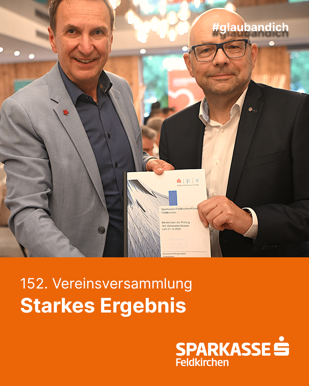 Zwei Männer stehen nebeneinander, einer hält ein Zertifikat mit dem Text '152. Vereinsversammlung Starkes Ergebnis'. Beide Männer sind formell gekleidet und scheinen zu lächeln. Der Hintergrund ist unscharf.
