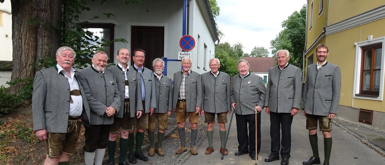 Eine Gruppe älterer Männer in traditioneller deutscher Kleidung steht auf einer Straße. Sie haben verschiedene Accessoires wie Stöcke und tragen Hüte. Ein Schild hinter ihnen steht 'Ausfahrt frei'.