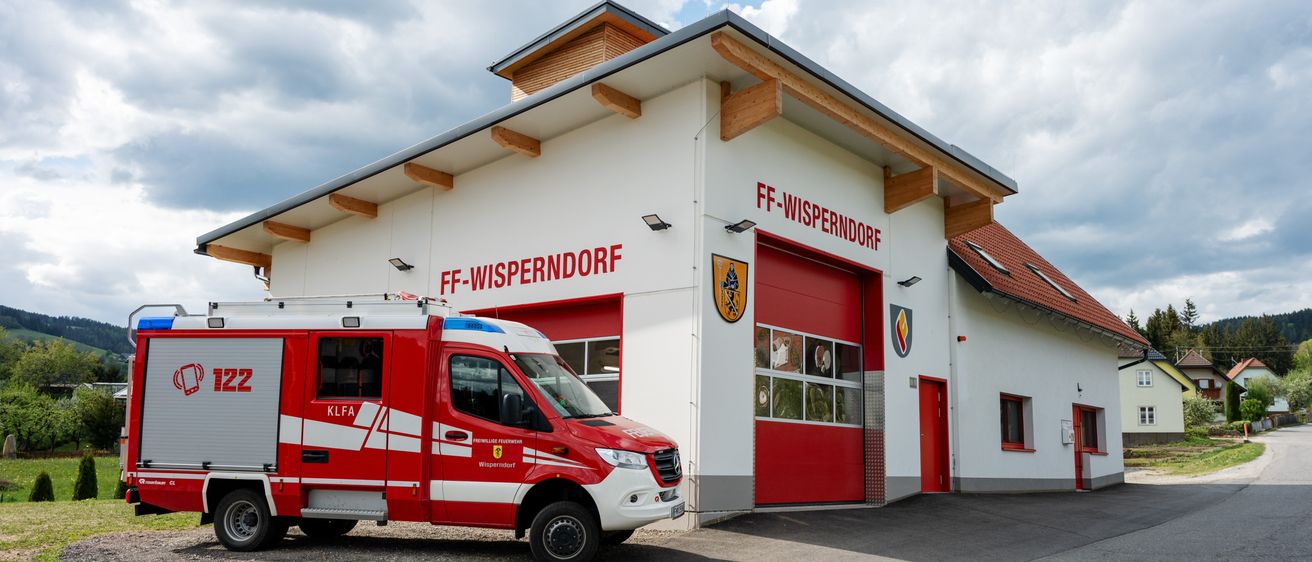 Ein roter Feuerwehrwagen steht vor der FF-WISPERNDORF-Feuerwache mit roten Garagentoren.