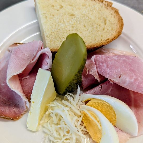 Ein Teller mit einem Sandwich, Schinken, Käse, Gewürzgurken und hartgekochten Eiern.