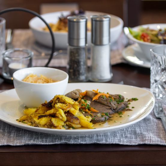 Ein Teller mit Fleisch, Kartoffeln und Gemüse auf einem Tisch mit Salz- und Pfefferstreuer und anderen Gerichten.