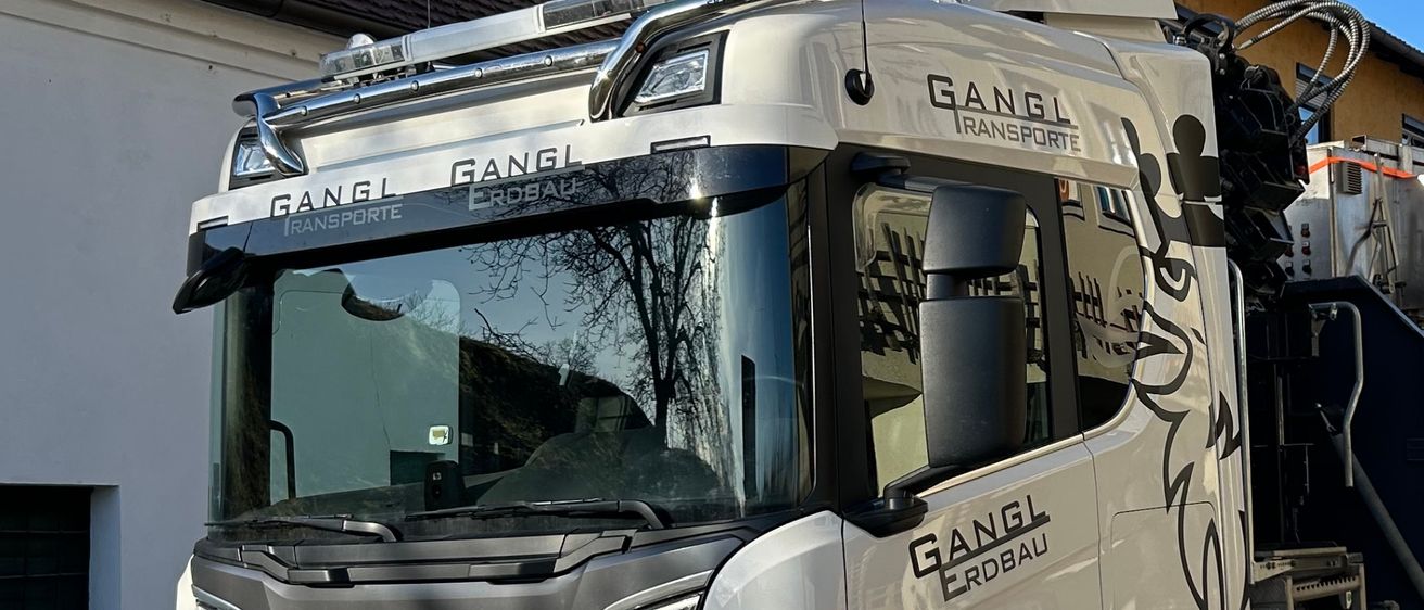 Ein weißer Scania-Lkw mit Logo und der Aufschrift 'GANGL' an der Seite ist vor einem Haus geparkt.