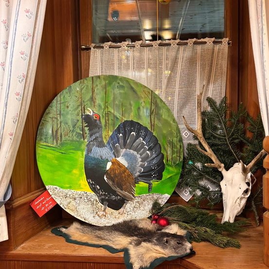 Ein Gemälde eines Auerhuhns mit offenem Schnabel, ausgestellt auf einem Fenstersims neben einem Weihnachtsbaum und einem Hirschschädel.