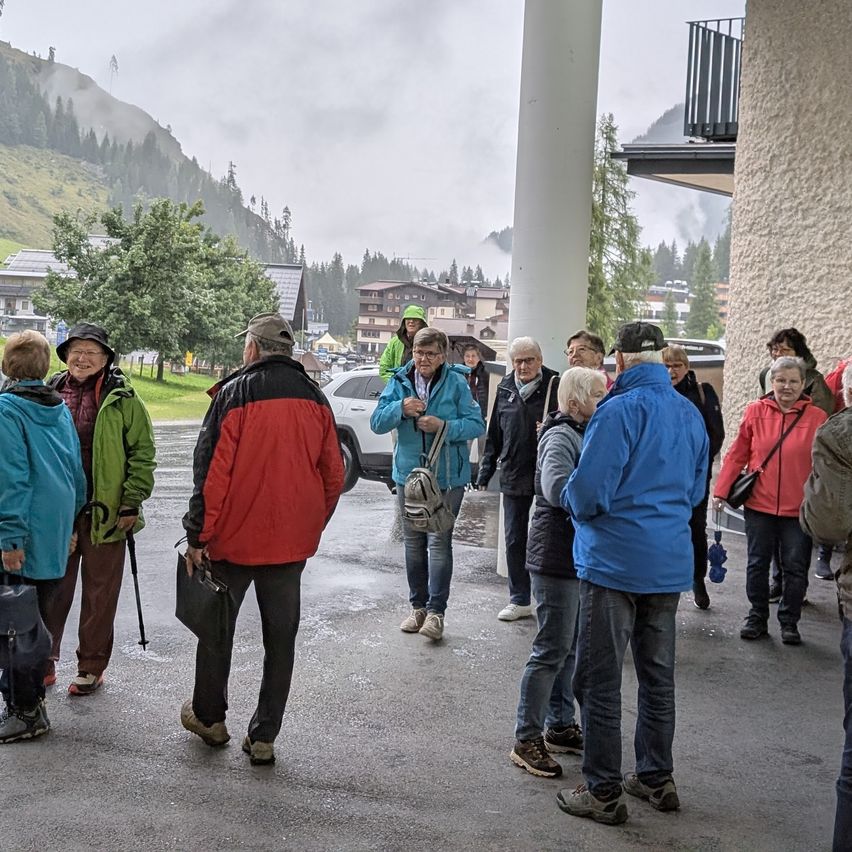 Eine Gruppe von Menschen in warmen Kleidungsstücken steht auf einem Parkplatz mit Bergen im Hintergrund.