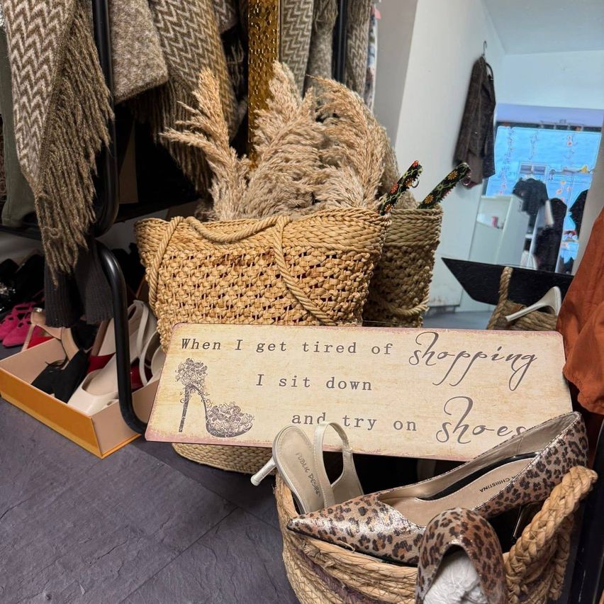 Ein Schild mit Schuhen darauf sagt: 'Wenn ich beim Einkaufen müde werde, setze ich mich hin und ziehe Schuhe an.' Leopardenprint-High-Heels sind in einem Korb.