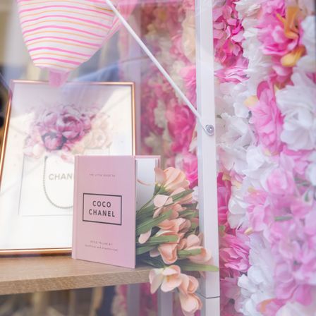 Eine pinke und weiße Blumendekoration mit einem Chanel-Buch und einer pinken Blumengestecke.