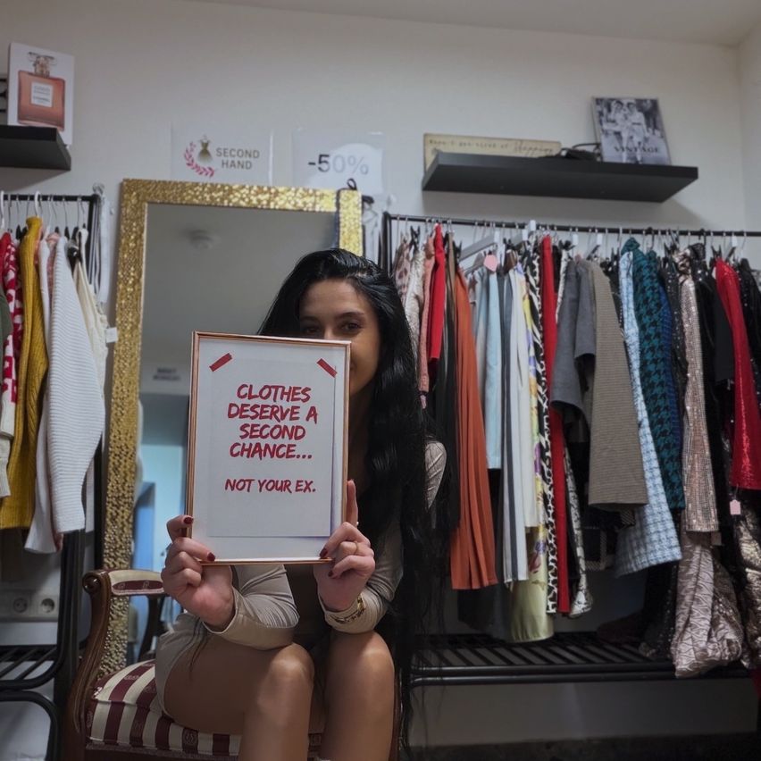 Eine Frau hält ein Schild mit der Aufschrift Kleidung verdient eine zweite Chance... Nicht deine Ex vor einem Kleiderständer.