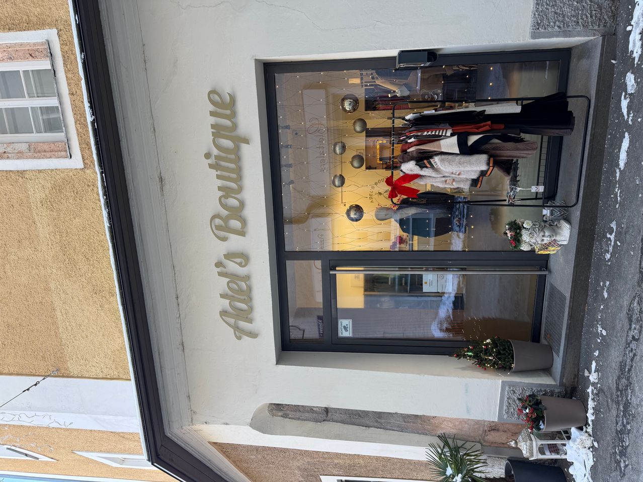 Ein Blick von oben auf Adel's Boutique, mit einem Glasfenster, durch das Kleidungsstücke zu sehen sind. Der Name des Geschäfts ist über dem Fenster auf der Wand angebracht.