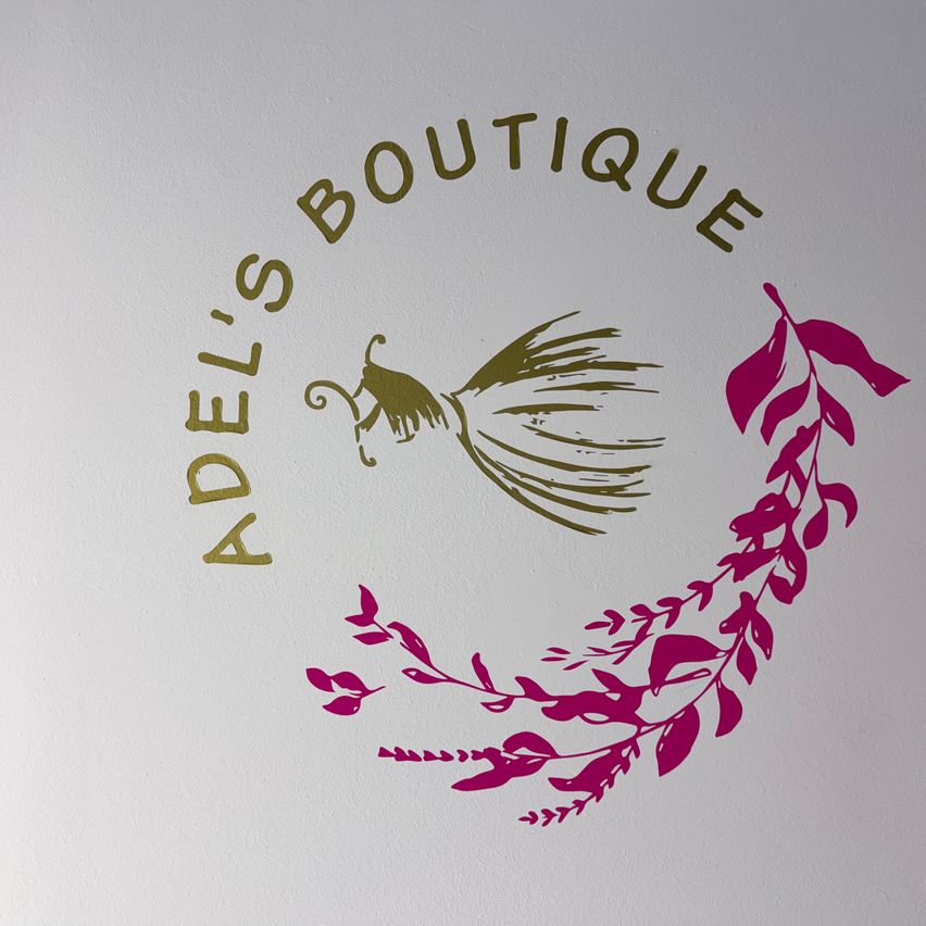 Das Bild zeigt das Logo von Adel's Boutique mit goldenem Text und einem stilisierten Blatt sowie einem Schmetterlingsdesign in Pink.