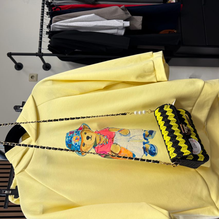 Ein gelbes Shirt mit einem Bärendesign darauf, das eine gelbe und schwarze Umhängetasche mit Perlen und einem dekorativen Muster zeigt.