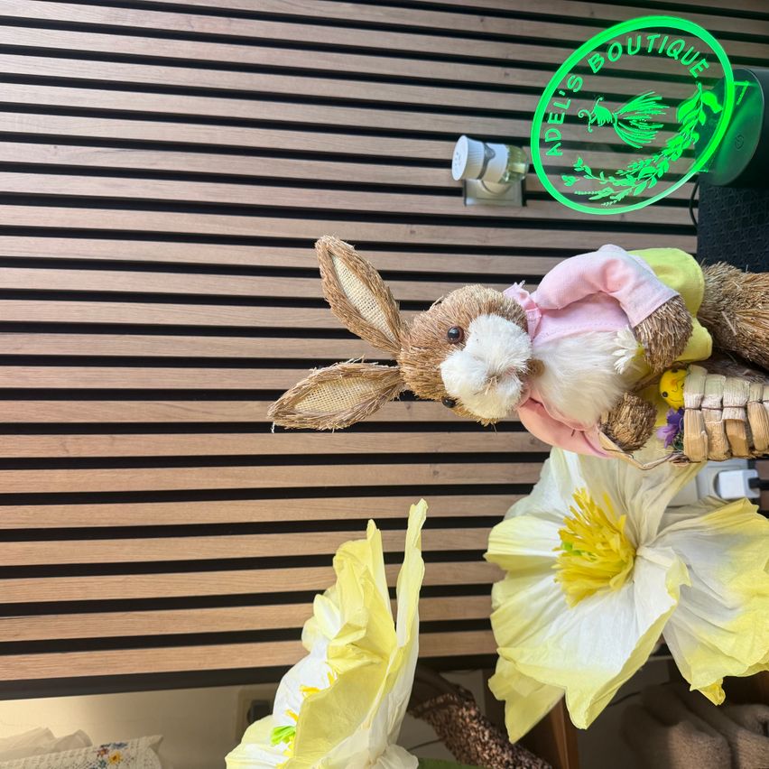 Ein Plüschhase sitzt über gelben Blumen vor einer Holzwand mit einem grünen Licht darüber.