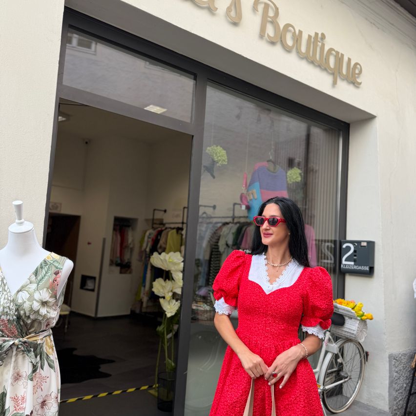 Eine Frau in einem roten Kleid steht vor einem Boutique mit einem Mannequin in einem Blumenkleid im Vordergrund.