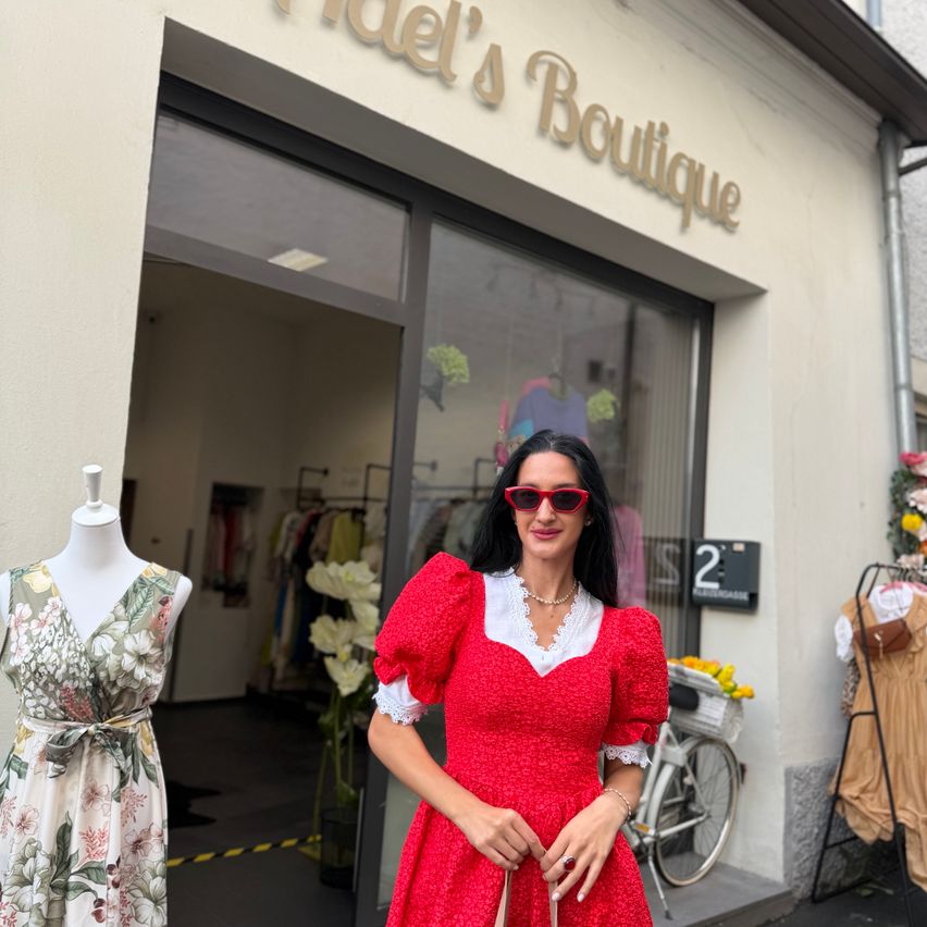 Eine Frau in einem roten Kleid steht vor einem Boutique mit einem Mannequin in einem Blumenkleid.