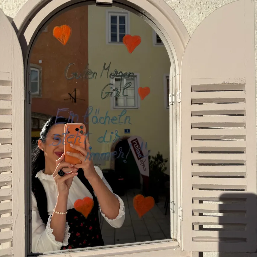 Eine Frau macht ein Selfie vor einem Fenster mit einem herzförmigen Aufkleber darauf.
