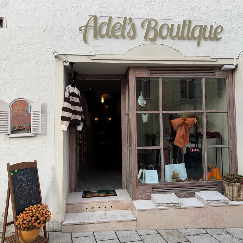 Der Eingang von Adel's Boutique, einem Bekleidungsgeschäft mit einem Kreidetafelschild und einem Topf mit orangefarbenen Blumen.