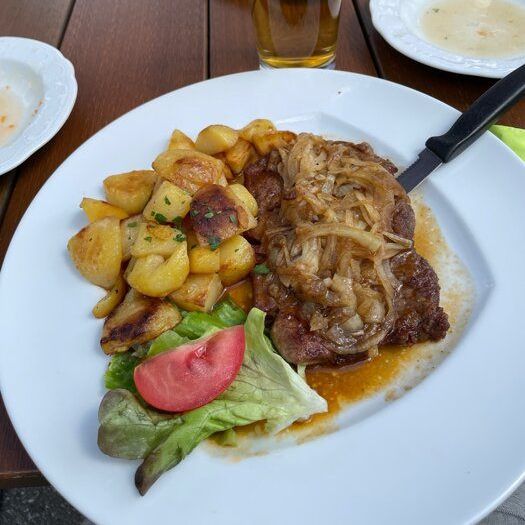 Ein Teller mit Steak, Kartoffeln und einem Glas Bier steht auf einem Holztisch mit anderen Gerichten.