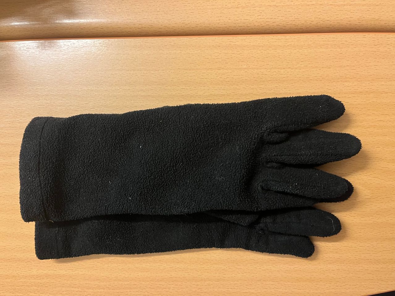 Ein Paar schwarze Handschuhe mit strukturierter Oberfläche, gefaltet und auf einer Holzoberfläche abgelegt.