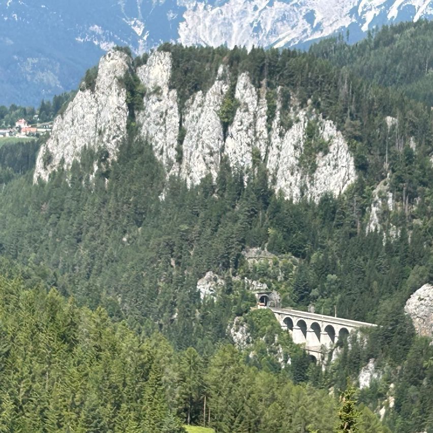Eine malerische Aussicht auf eine bergige Region mit einer Brücke, die in einen steilen Hang gebaut wurde, umgeben von dichten grünen Wäldern.