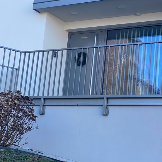 Ein modernes Haus mit Balkon hat ein Metallgeländer. Ein Kranz hängt an der Tür.