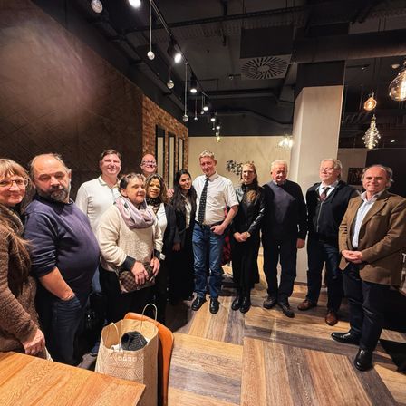 Eine Gruppe von Menschen steht in einem modernen Raum mit Holzböden, in Winterkleidung. Sie scheinen für ein Foto zu posieren.