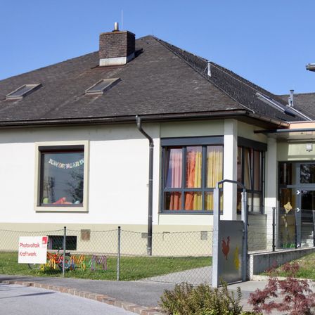 Außenansicht eines Gebäudes mit Glasfenstern, einem Schornstein und einem Garten mit bunten Pflanzen.