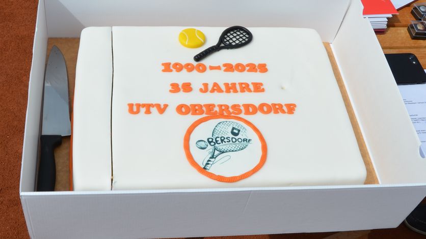 Ein weißer Kuchen dekoriert mit einem Tennisball, einem Tennisschläger und oranger Schrift, die '1990-2025 35 Jahre Utv Obersdorrf' lautet.