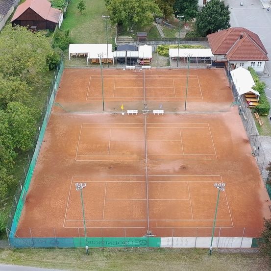 Ein Luftbild eines Tennisplatzes mit mehreren Tennisplätzen, Bänken und Straßenlaternen. Der Platz ist leer.
