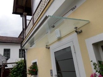 Ein gelbes Haus mit einem Glasvordach über der Eingangstür, das einen Balkon darüber und einen kleinen Garten mit Blumen davor aufweist.
