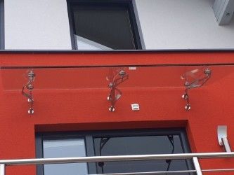Ein rotes Gebäude mit einer Glasbrüstung und Metallverzierungen über dem Eingang. Über der Brüstung befinden sich zwei Glasfenster.