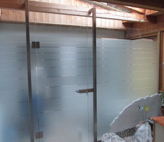 Ein Innenbereich mit einer Glasdusche, einer Holzdecke und einer Wand. Ein Topf mit einer Pflanze steht rechts.