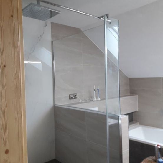Ein Badezimmer mit einer Glasdusche, einer Holzbank und einer Badewanne. Die Wände und der Boden sind mit grauen Fliesen verkleidet.