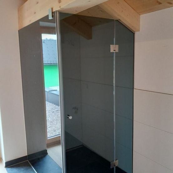 Ein moderner Duschbereich mit einer Glaswand und schwarzem Fliesenboden, offen zu einem Raum mit einer Holzdecke und weißen Wänden.