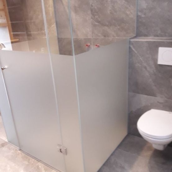 Ein Badezimmer mit einer Glasdusche, gefliesten Wänden, einer Toilette und einem montierten weißen Schalter.