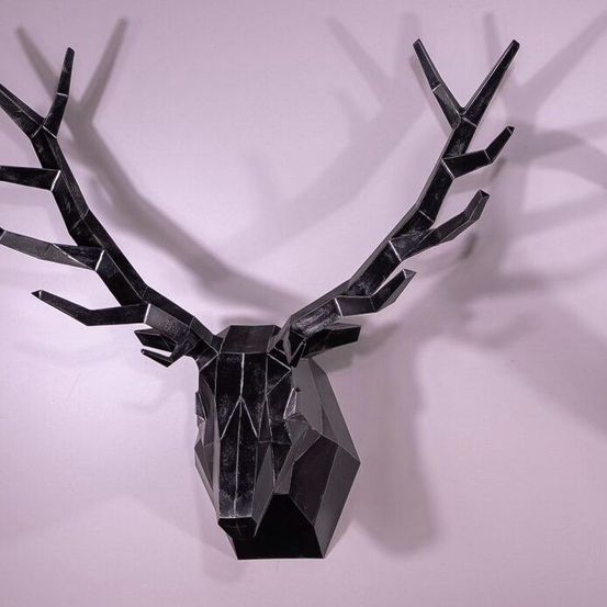 Zwei geometrische Tierköpfe an einer rosa Wand montiert. Der linke ist ein schwarzer Hirschkopf, der rechte ein silberner Gazellenkopf. Beide Köpfe sind abstrakt und modern.