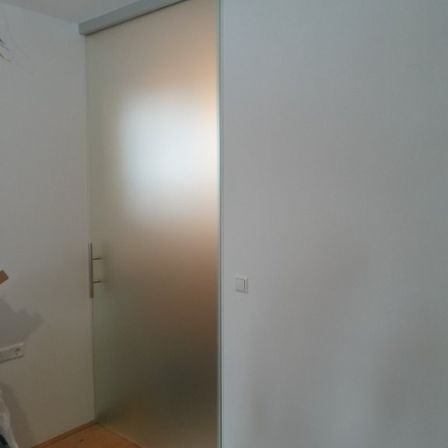 Ein Raum mit einer weißen Wand, einer Schiebetür aus Glas und einem weißen Schalter an der Wand.