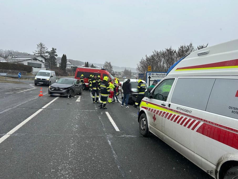 Rettungskräfte kümmern sich um einen Verkehrsunfall auf einer Straße, wobei ein Krankenwagen und Feuerwehrleute anwesend sind.