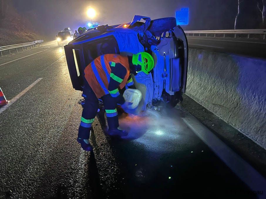 A safety officer inspects a flipped vehicle on the side of the road at night.