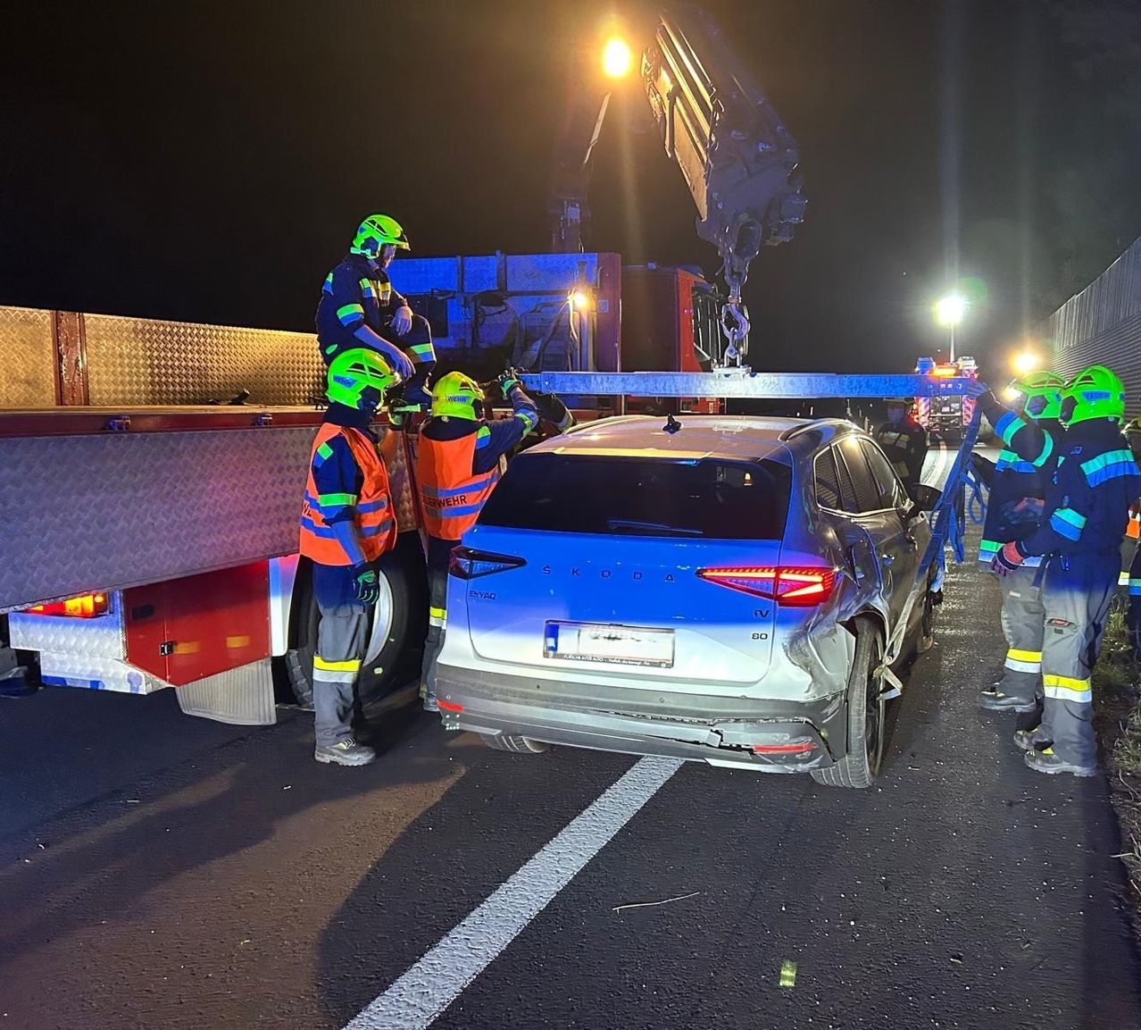 Rettungskräfte in reflektierenden Westen und Helmen benutzen einen Kran, um ein beschädigtes Auto nachts von der Straße zu heben.
