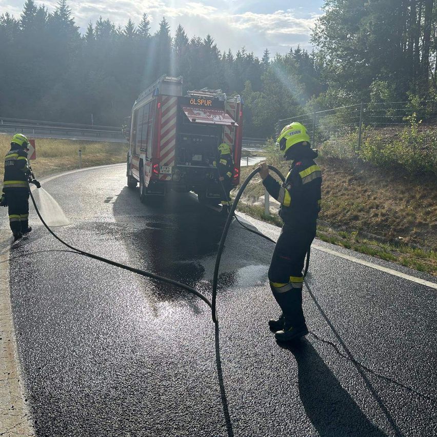 Feuerwehrleute sprühen Wasser auf eine Straße, ein Feuerwehrwagen steht in der Nähe.