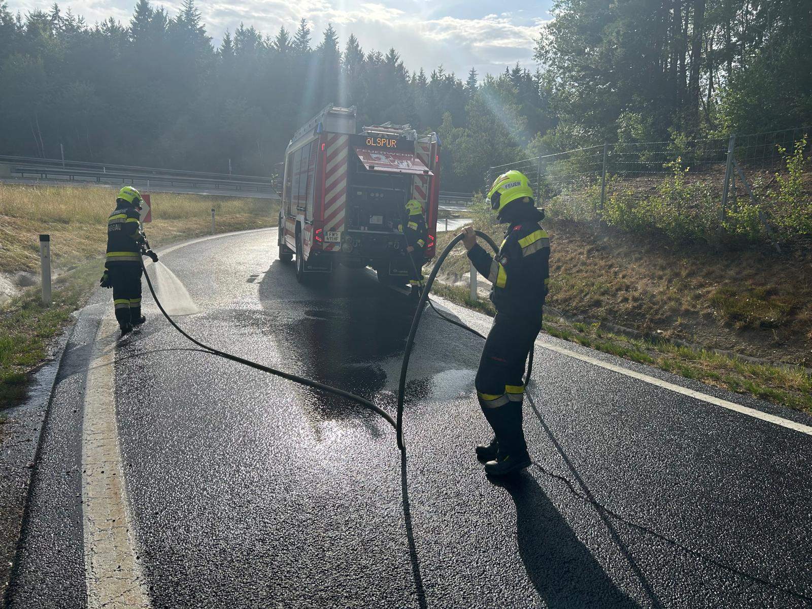 Feuerwehrkräfte reinigen Ölspur auf Straße mit Löschfahrzeug und Wasserschlauch