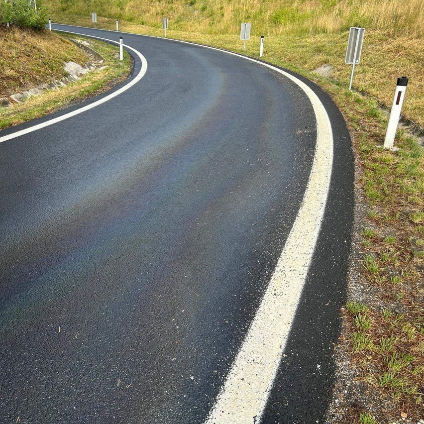 Eine kurvenreiche Straße mit einer weißen Linie auf der Seite, umgeben von Gras und kleinen Pfosten.