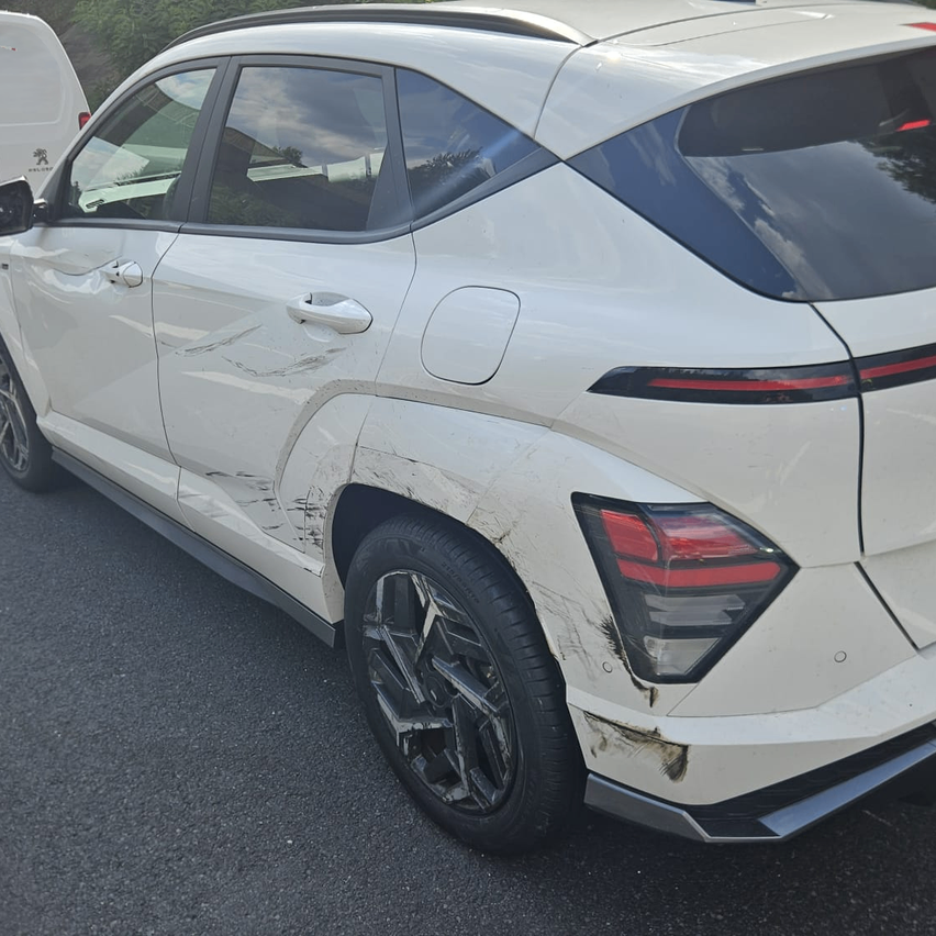 Ein weißer SUV mit sichtbaren Schäden am Heckstoßfänger und der Seite, auf einer Straße geparkt.