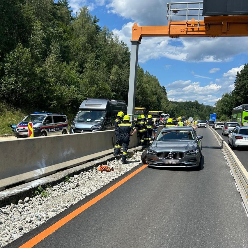 Rettungskräfte in gelben Helmen helfen einem beschädigten Auto auf einer Autobahn, mit einem Polizeiwagen und anderen Fahrzeugen in der Nähe.