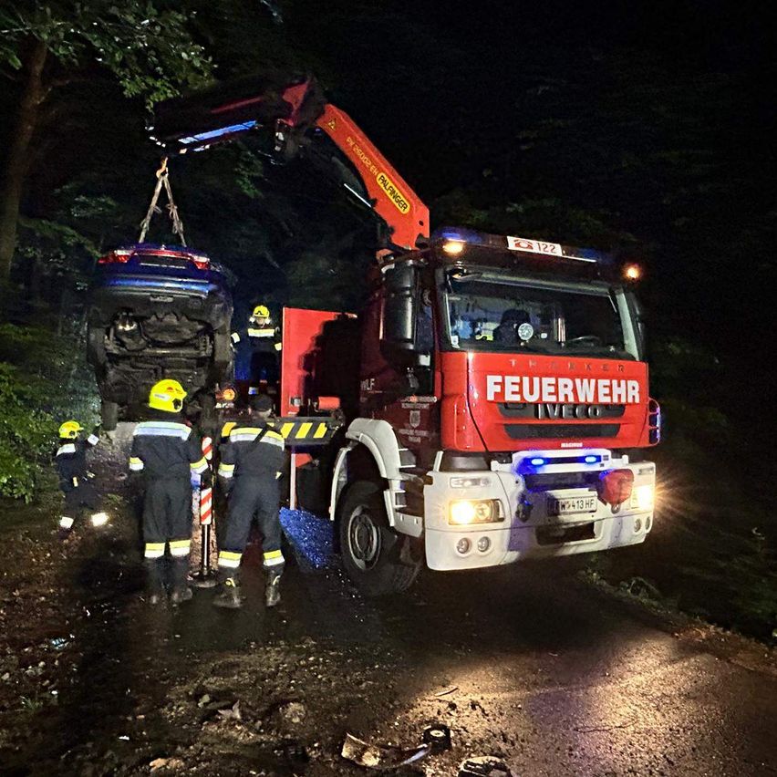 Feuerwehrleute benutzen einen Kran, um ein beschädigtes Auto nachts von der Straße zu heben.