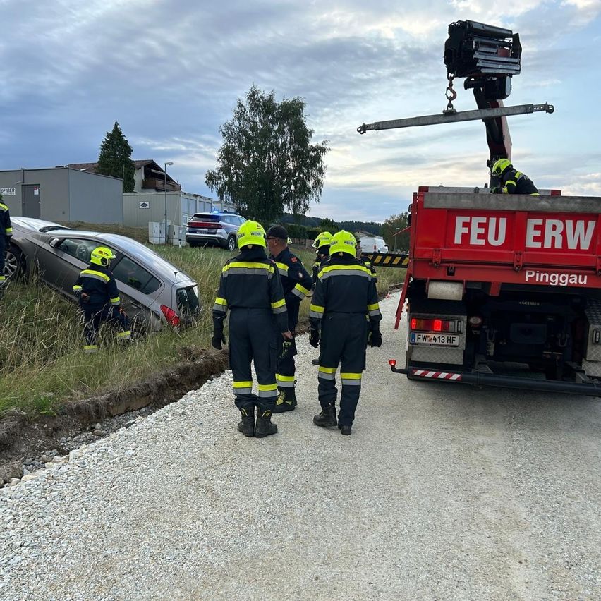 Feuerwehrleute in gelben und schwarzen Uniformen kümmern sich um ein umgekipptes Auto am Straßenrand, in der Nähe befindet sich ein roter Feuerwehrwagen mit der Aufschrift 'FEU ERW'.