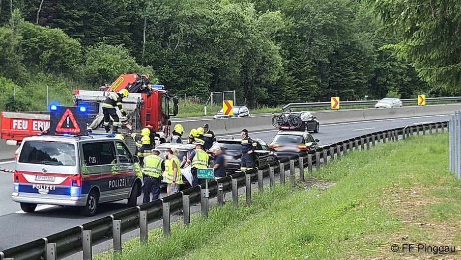 Emergency services are attending to a car accident on a highway. Firefighters are on top of a truck, and police are standing nearby.